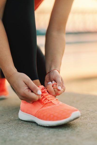 Close up of sporty woman tying shoelace while kneeling outdoor, In background bridge. Fitness outdoors concept.